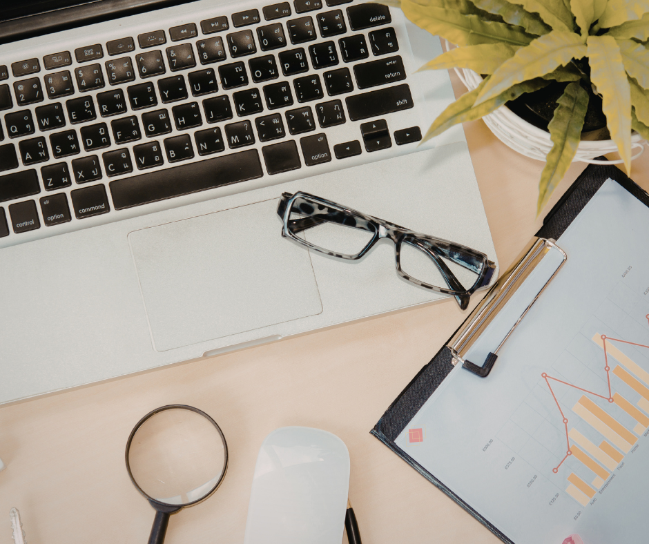Desktop photo with a laptop, clipboard, and glasses.