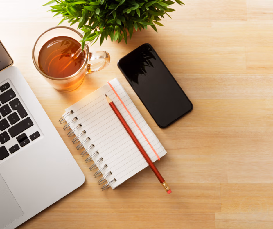 Photo of a desk with a laptop, notebook, phone and drink